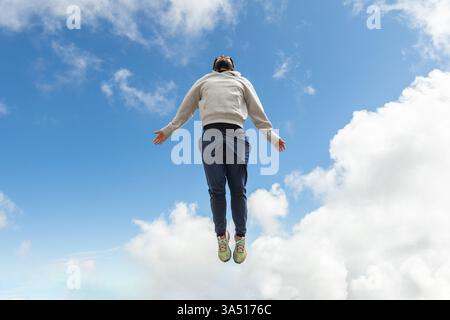 From below shot of a casual male jumping with hands apart against a cloudy blue sky near Nevado de Toluca, Mexico. This energetic travel lifestyle image conveys freedom, adventure, and outdoor activity in daylight. Ideal for tourism, summer, and motivational branding. Stock Photo