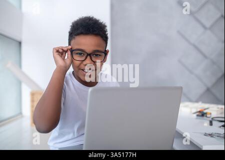 A connected teen sits at a laptop, looking engaged with the screen. The indoor setting conveys youth lifestyle and technology use. Ideal for articles about digital hobbies, online learning, and student tech. Stock Photo