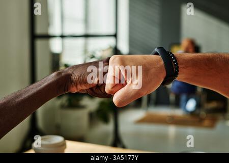 Close-up of a fist bump between two young intercultural businessmen, celebrating a successful deal. The moment highlights teamwork, partnership, and achievement in a diverse corporate setting. Ideal for business success, collaboration, and multicultural teamwork themes. Stock Photo