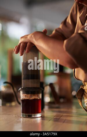 Asian female barista making coffee with an Aeropress in a coffee shop. This lifestyle shot highlights coffee culture, morning routine and skilled barista work. Stock Photo