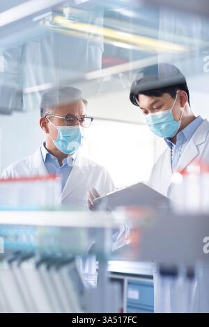 Two Chinese researchers discuss in a laboratory. They are surrounded by lab equipment, showcasing teamwork in medical research and biotechnology. Ideal for science and healthcare themes, including laboratory work and biotechnology. Stock Photo