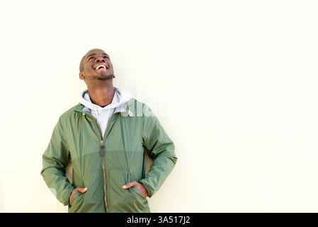 Portrait of a happy African American man laughing beside a wall. This casual, confident head-and-shoulders shot with a bright, natural background, perfect for lifestyle and confidence branding. Great for advertising, fashion, and wellness campaigns featuring smiling male models. Stock Photo