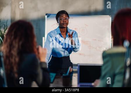 Multicultural female manager leads a briefing with her team, discussing business strategy and marketing ideas in a meeting room. Captures leadership, teamwork and professional office dynamics. Ideal for corporate communications and business planning visuals. Stock Photo