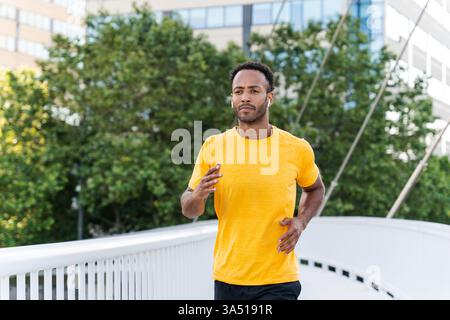 A fit Black Hispanic male athlete trains outdoors in the city, performing a functional cardio workout to build strength. The scene captures energy and determination amid an urban backdrop. This dynamic fitness image supports sportswear, training, and active lifestyle campaigns. Stock Photo