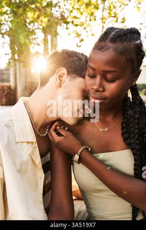 Glad African American female smiling with closed eyes and touching face of young boyfriend during romantic date on sunny summer day on street Stock Photo