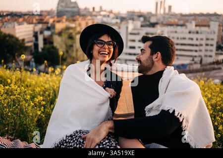 Stylish woman wearing eyewear chats with her bearded partner in a vibrant urban setting with blooming flowers. The scene blends fashion, lifestyle and romance, ideal for couple and city life themes. Stock Photo