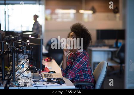 Portrait of a confident African American woman in a modern open office. A professional, cheerful scene featuring a stylish workspace with a laptop and smartphone, conveying success and focus. Ideal for corporate lifestyle, work life balance, and female entrepreneurship themes. Stock Photo
