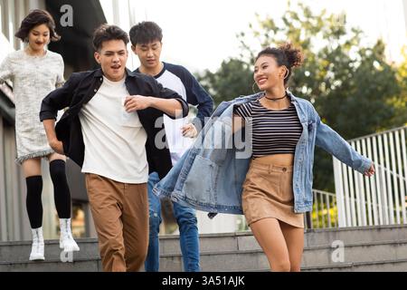 Group of Chinese friends running downstairs in a sunny city scene. This energetic lifestyle image captures friendship, youth, and urban vitality. Ideal for city life, travel, and social campaigns. Stock Photo