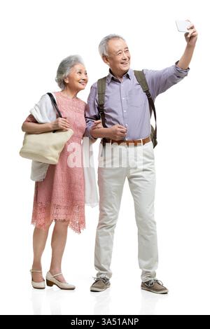 Cheerful Chinese senior couple taking a selfie in a studio setting. This upbeat portrait pairs well with travel, aging well, and lifestyle campaigns, with copy space for branding. Stock Photo