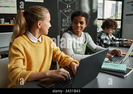 Classmates in an IT class collaborate at a table, typing on laptops. The scene highlights learning, technology, and hands on digital skills. Great for education, computer literacy, and classroom teamwork themes. Stock Photo
