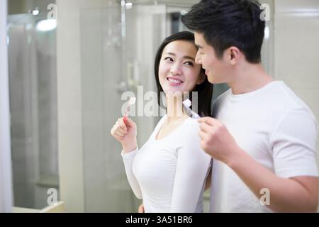 Happy young Chinese couple brushing teeth in a Beijing apartment bathroom. The scene captures a cheerful domestic moment and morning dental hygiene in a modern home setting. Suitable for lifestyle campaigns about family, morning routines, or healthy habits. Stock Photo