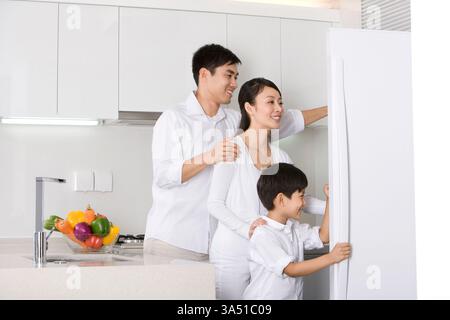 Chinese family opens the refrigerator in a modern kitchen, capturing everyday domestic life. The scene emphasizes togetherness and healthy eating in a bright home environment. Great for campaigns about family meals and modern living, with copy space available. Stock Photo