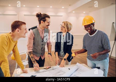 Cheerful Black woman laughs with a Caucasian colleague while collaborating at a table in the office. This image conveys teamwork, diversity, and productive workplace interaction. Stock Photo