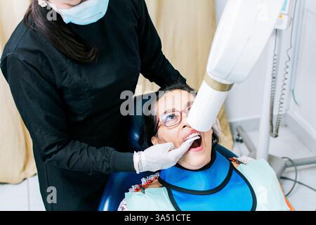 Nicaraguan female dentist wearing gloves performing dental x-ray to senior female patient lying on dental chair in clinic Stock Photo