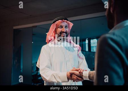 An elderly Arab man shakes hands with a businessman after a successful meeting. The image conveys professional collaboration and dealmaking in a corporate setting. Ideal for business partnerships, Middle Eastern markets, and executive networking imagery. Stock Photo