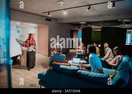 Older Muslim businesswoman presenting a project to a diverse team in a modern office. Emphasizes leadership, inclusion, and collaboration in business. Ideal for corporate diversity imagery. Stock Photo