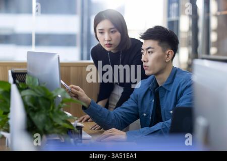 Chinese IT experts collaborate at a computer in a modern office. Great for technology, IT services, and collaboration in Chinese or Asian market contexts. Stock Photo