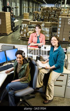 A group of women sits at a front desk inside a busy warehouse, reflecting a diverse and collaborative team. The scene emphasizes logistics, packaging, and warehouse operations with a positive, professional atmosphere. Ideal for content on female employees, warehouse staff, and empowerment in logistics and retail. Stock Photo