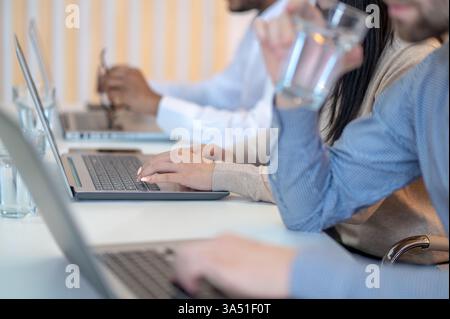 Cropped photo of three diverse employees sitting at a table and typing on laptops. This workplace scene highlights teamwork and collaboration, ideal for business, technology or startup features. Great for articles on meetings, planning and productive teams. Stock Photo