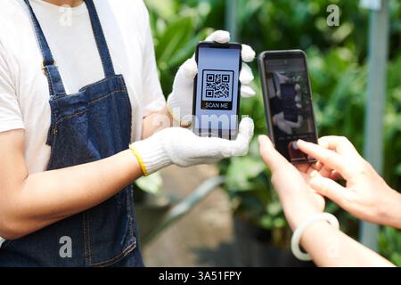 Hands operate a smartphone screen displaying a QR code used for payment at a gardening centre. This scene demonstrates contactless payment, wireless technology, and retail in horticulture. Stock Photo