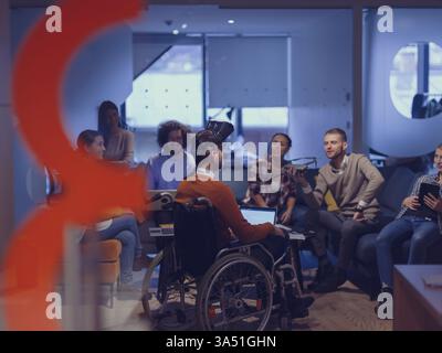In a modern open space coworking office, a disabled businessman in a wheelchair joins a team meeting using virtual reality goggles with drone assistance. The scene emphasizes inclusion, innovation and collaborative work in a futuristic workplace. Stock Photo