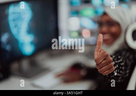 Young Afro American Muslim businesswoman wearing a scarf in a bright, creative office. She is pictured with a big screen in a modern startup workspace. This diverse, professional scene works for leadership, education, and workplace branding. Stock Photo