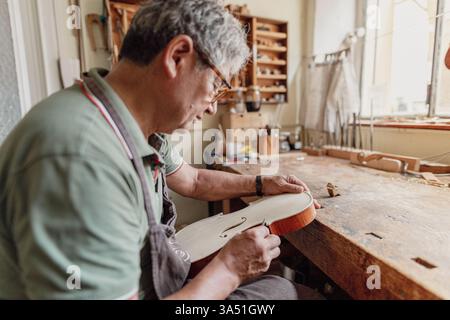 Violin maker at work in a traditional Italian workshop, focused on craftsmanship. An artisan luthier shaping violins with precision. Great for stories about handmade instruments, craftsmanship, and Italian artistry. Stock Photo