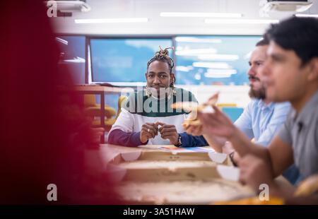 Diverse group of office workers sharing pizza during a lunchtime break. A casual, friendly team moment that showcases collaboration and a relaxed workplace vibe. Ideal for features on teamwork, office culture, and staff meals. Stock Photo