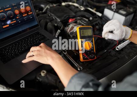 Closeup of an Asian male mechanic using a multimeter to inspect a car engine in a workshop. The hands and precision tools highlight automotive expertise and service work. Ideal for car repair, maintenance and vehicle diagnostics in automotive contexts. Stock Photo