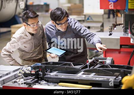 Chinese male engineers checking machinery in a factory setting. A clear industrial scene highlighting manufacturing, quality control and teamwork. Suitable for engineering, production and workplace imagery. Stock Photo