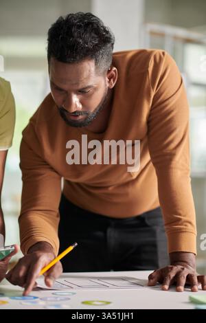 UX designer discussing app interface variants with colleagues around a table in a workspace. This modern tech scene highlights teamwork, creativity, and digital product development for business and marketing campaigns. Ideal for software, UX UI, and innovation branding. Stock Photo