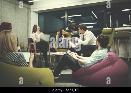 Diverse startup team working on laptops and tablet sitting on chairs and brainstorming new ideas in the office. This modern group scene is ideal for entrepreneurship, innovation and business teamwork content. The mix of genders and backgrounds reflects a collaborative, creative workplace. Stock Photo