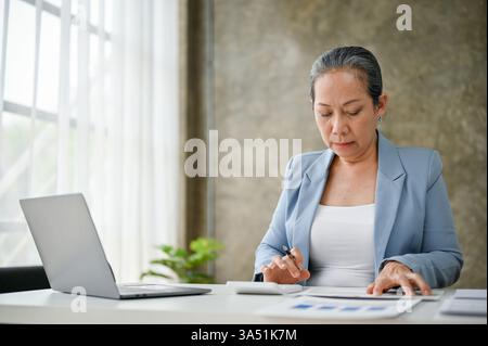 Professional Thai businesswoman reviews documents in a modern office. Confident corporate portrait suitable for finance, leadership, and corporate communications. Ideal for business materials, team branding, and professional services. Stock Photo