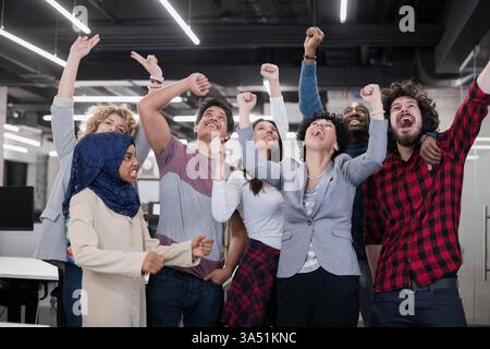 Multiethnic software development team celebrating success in a modern startup office. They stand together, looking at the camera with smiles, conveying teamwork and achievement. Perfect for business, tech, and corporate culture imagery. Stock Photo