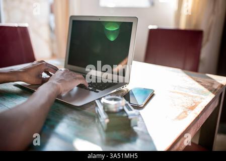 Professional and relatable remote work scene featuring a woman working from home at a computer. She types on a laptop at a tidy desk with a notebook nearby, reflecting a modern home office vibe. Stock Photo