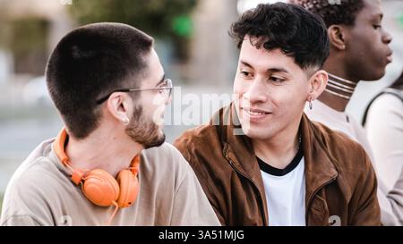 Hispanic and Caucasian male college students chat while sitting outdoors on campus. A diverse, campus-life moment that captures friendship, conversation and multicultural study environments. Ideal for features on university life, student collaboration and multicultural education. Stock Photo