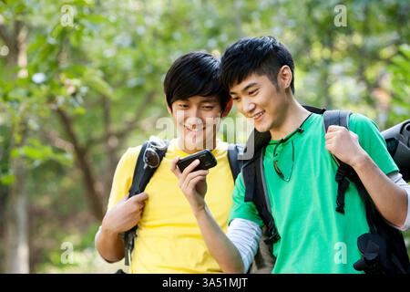 Chinese hikers using a mobile phone with GPS while exploring outdoors. Two young men share a moment of discovery on a hiking trip, highlighting outdoor adventure and modern navigation. Suitable for travel, nature, and wellness campaigns emphasizing active lifestyles. Stock Photo
