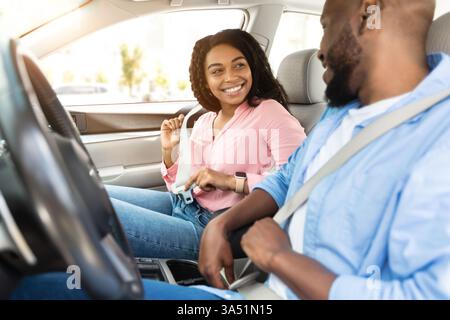 Smiling African American couple fastens seat belts before driving in a stylish city car. The image communicates safety, responsible travel, and family or couple moments behind the wheel. Perfect for articles about road safety, urban driving, and premium automotive experiences. Stock Photo