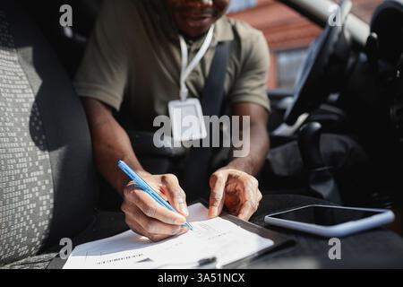 Close-up of a Black delivery man filling in papers and forms in a van, with copy space. Ideal for logistics, courier services, online shopping campaigns, and business communication. Stock Photo