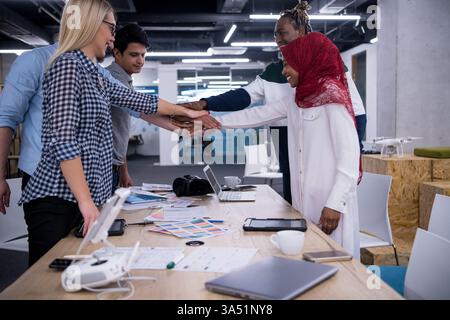 Smiling diverse group of business people put their hands together to celebrate success in the office. This teamwork moment highlights collaboration and a positive corporate culture. Stock Photo