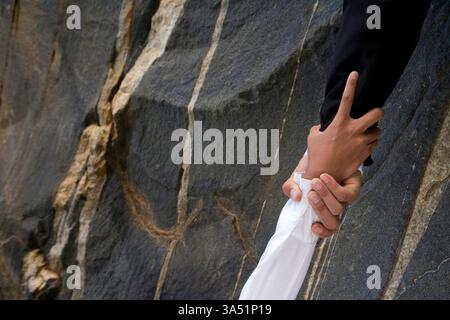 Two people cooperate on a rock climbing challenge outdoors, demonstrating teamwork and mutual support in an adventurous setting. The scene emphasizes effort, grip on the rock face, and conquering adversity with careful technique and a steady hand. Copy space around the subjects makes it suitable for branding or messaging. Stock Photo