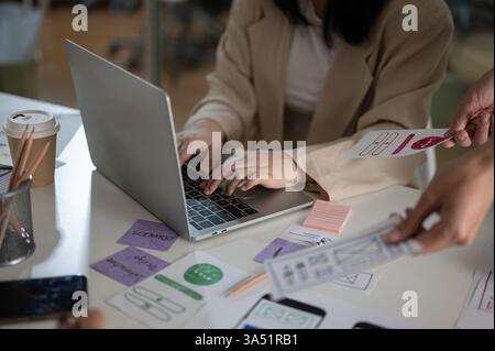 Professional Asian female graphic designer collaborates with her team in a modern office, working on a laptop during a design meeting. The image emphasizes collaboration, creativity and UX UI planning in a contemporary workplace. Ideal for design studios, tech teams and marketing campaigns. Stock Photo