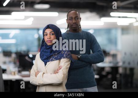 Portrait of a Black Muslim female software developer with a male colleague in a modern startup office. The scene highlights diversity, collaboration, and tech innovation. Stock Photo