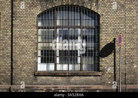 A no stopping sign casts a shadow on the brick wall on the disused industrial site of an old factory with a barred window Stock Photo
