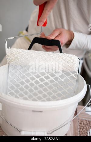 Person applying paint using a roller in a white bucket during a home renovation project Stock Photo