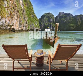 Two convenient comfortable guest sun loungers and a bedside table are worth on a wooden platform. An excellent review on the beach and native boats. C Stock Photo