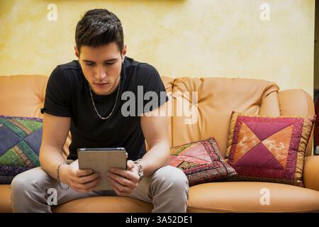 Handsome young man at home, using tablet PC sitting on a couch at home Stock Photo