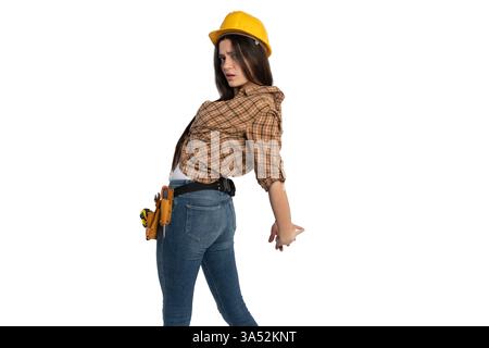 A female construction worker wearing a yellow hard hat and tool belt leans backward, stretching her back to relieve tension. Workplace safety and phys Stock Photo