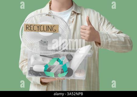 Woman with electronic waste for recycling in container showing thumb-up on green background Stock Photo