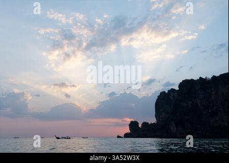 Sunset over the Andaman Sea, with longtail boats drifting near the towering limestone cliffs of Tonsai Stock Photo